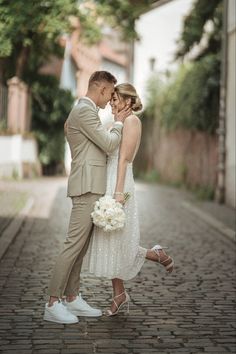 a bride and groom are standing together on the cobblestone street in their wedding attire