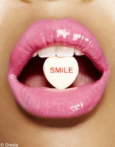 a woman's lips with a white heart shaped pill in the mouth that says smile