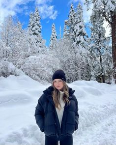 a woman standing in the snow with her hands on her hips and trees behind her