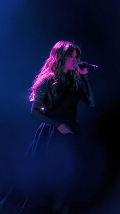 a woman standing on top of a stage holding a microphone in her hand and singing