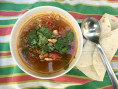 a bowl of soup with tortilla chips and cilantro on the side