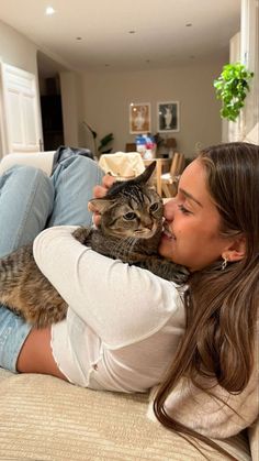 a woman laying on top of a couch holding a cat