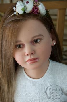 a close up of a doll with flowers in her hair and wearing a white shirt