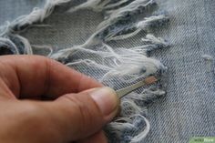 someone using scissors to cut the fabric off of a pair of denim jeans with fraying