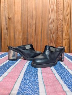 Elevate your shoe game with these stunning vintage Clash leather clogs, a true testament to 90s fashion. Designed with a bold, chunky heel and sleek black leather, these clogs are perfect for anyone looking to add a touch of edgy sophistication to their wardrobe. Key Features: Brand: Clash Era: 1990s, Made in Spain Material: Genuine leather upper with sturdy synthetic sole Color: Classic black with a metallic silver block heel Size: UK 5 (Approx. EU 38, US 7) Insole: 24cm Heel Height: 9cm Striki Modern Streetwear Clogs With Round Toe, Modern Clogs With Round Toe For Streetwear, Modern Round Toe Clogs For Streetwear, Modern Slip-on Clogs For Streetwear, Closed Toe Leather Heels For Streetwear, Leather Closed Toe Heels For Streetwear, Retro Leather Platform Mules, Black Closed Toe Clogs With Sculpted Heel, Retro Closed Toe Leather Mules