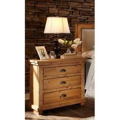 a bed room with a lamp and a wooden dresser next to a stone wall in the background