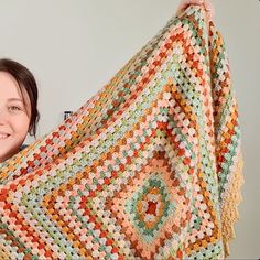 a woman holding up a crocheted blanket in front of her face and smiling at the camera