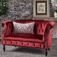 a red couch sitting on top of a rug in front of a brick wall next to a potted plant