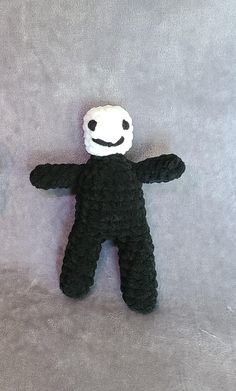 a crocheted black and white teddy bear laying on a gray surface with its eyes closed