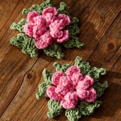 two crocheted pink flowers sitting on top of a wooden table next to each other