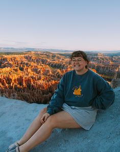 a woman sitting on the edge of a cliff