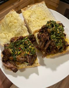 two pieces of bread with meat and greens on them sitting on a plate next to another piece of bread