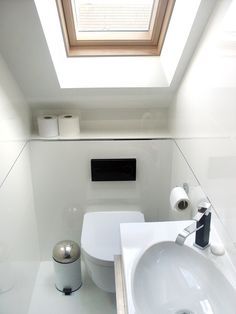 a white bathroom with a skylight above the sink and toilet paper dispenser