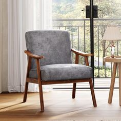 a chair sitting in front of a window next to a table with a lamp on it