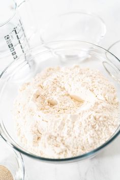 a glass bowl filled with flour next to a measuring cup on a white counter top