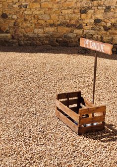 a wooden crate sitting on top of gravel next to a stone wall with a sign