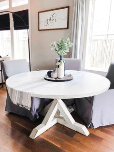 a white table with two chairs and a vase on it in front of a window