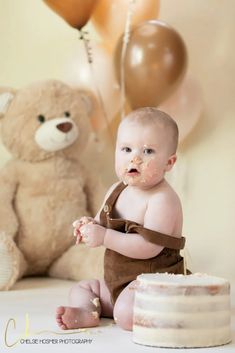 a baby sitting in front of a cake and teddy bear