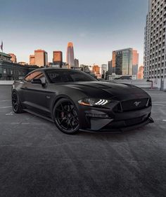 a black mustang parked in a parking lot with the city skyline in the back ground