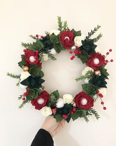 a hand holding a christmas wreath with red and white flowers on the front, greenery around it