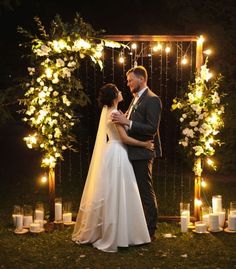 a bride and groom standing in front of a wedding arch with lit candles on it