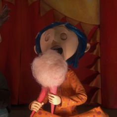 a small doll with blue hair sitting on top of a floor next to a red curtain