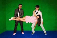 two men and a woman posing in front of a green screen with one holding the leg up