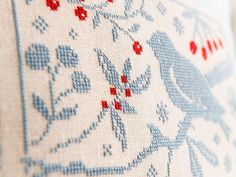 a close up view of a cross stitch pattern on a white cloth with red and blue flowers