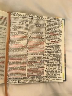 an open bible on a bed with white sheets and writing in red, black, and green