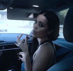 a woman sitting in the driver's seat of a car with her hand up to her lips