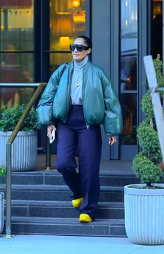 a woman walking down the street wearing a green jacket and yellow socks with her hands in her pockets