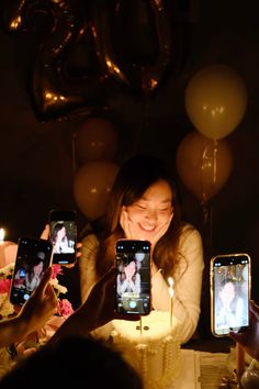 a woman holding up two cell phones in front of a cake with candles on it