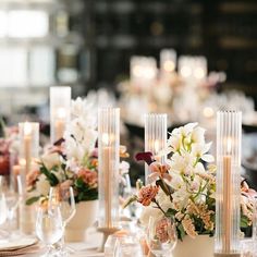 the table is set with white and pink flowers in vases, candles, and wine glasses