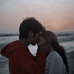 a man and woman are kissing on the beach at sunset, with waves in the background