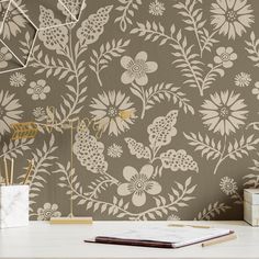 a desk with a book, pen and notebook on it next to a flower wallpaper