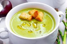 a white bowl filled with soup and croutons on top of green asparagus