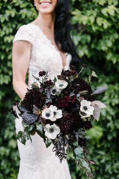 a woman holding a bouquet of flowers on her wedding day in front of greenery