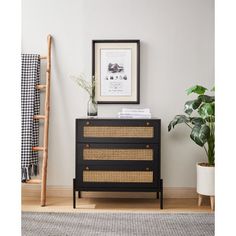 a black dresser with wicker drawers in front of a white wall and potted plant