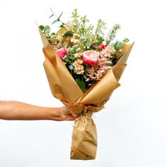 a person holding a bouquet of flowers wrapped in brown paper