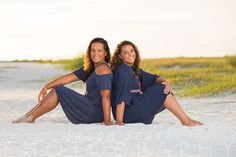 two young women sitting on the beach in matching blue outfits and smiling at the camera