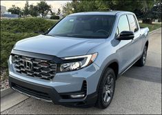 the front end of a gray honda passport parked on a street with bushes in the background