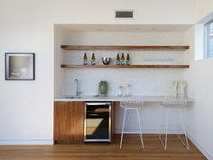 an empty kitchen with white walls and wooden shelves, two bar stools in the foreground