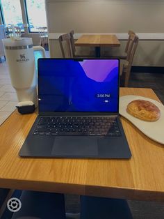 an open laptop computer sitting on top of a wooden table next to a plate of food