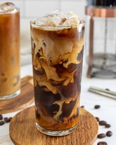 an iced drink with ice and coffee beans on a wooden coaster next to two glasses