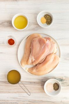 raw chicken on a white plate surrounded by spices and seasoning in small bowls next to it