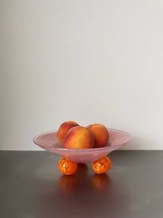 three oranges sitting in a bowl on top of a black table next to a white wall