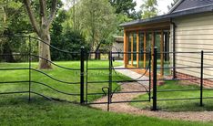 a black iron fence in front of a house with grass and trees around the yard