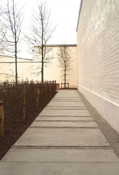 a white brick wall and sidewalk with trees in the backgrounge, next to it