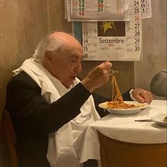 an old man sitting at a table eating spaghetti with chopsticks in front of him