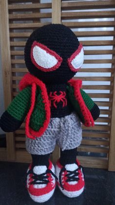 a crocheted stuffed animal with red and green eyes, black jacket and white pants